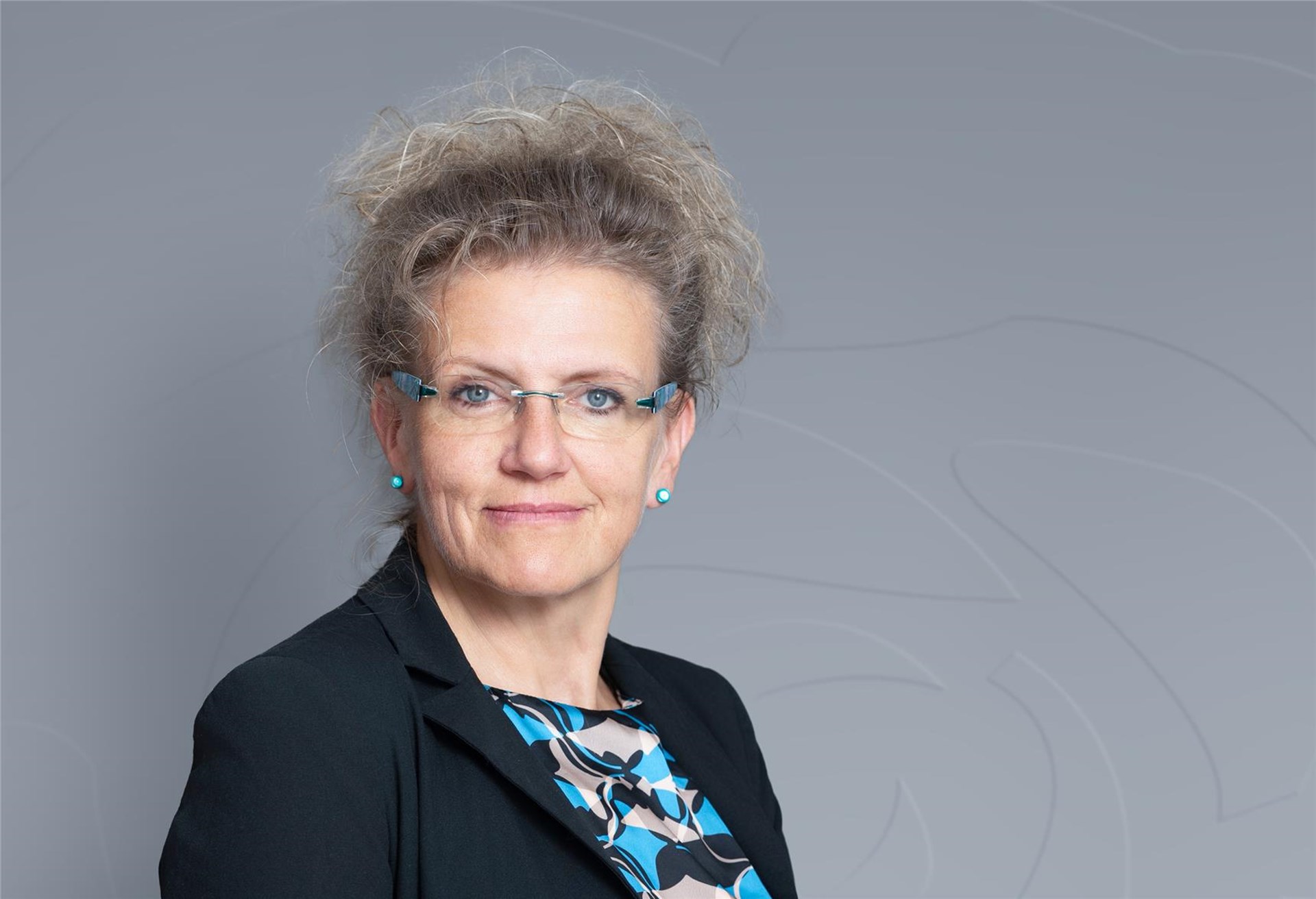 Frau mittleren Alters mit blonden hochgesteckten Haaren und einer Brille lächelt in die Kamera
