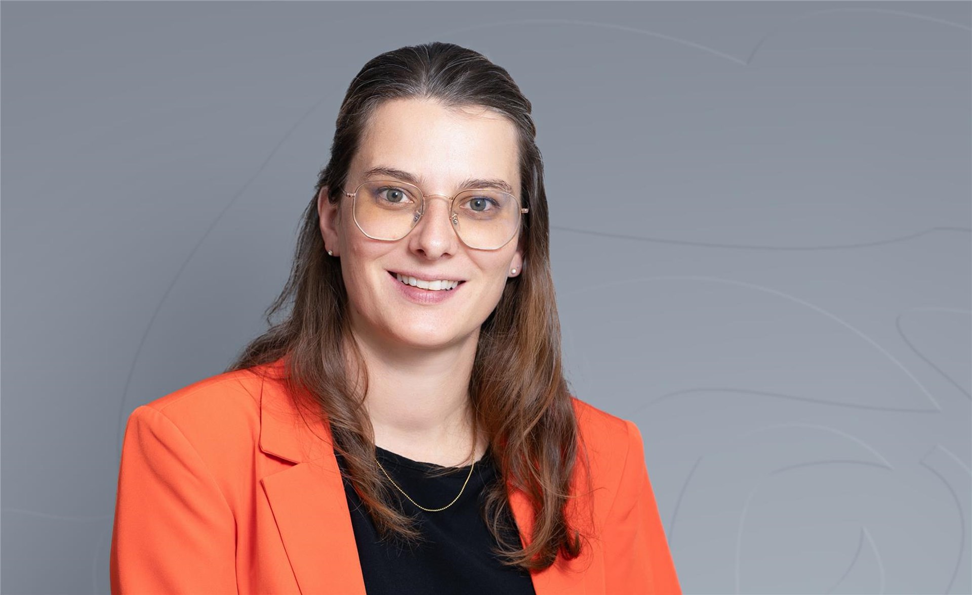 Junge Frau mit langen dunklen Haaren und einer Brille lächelt in die Kamera