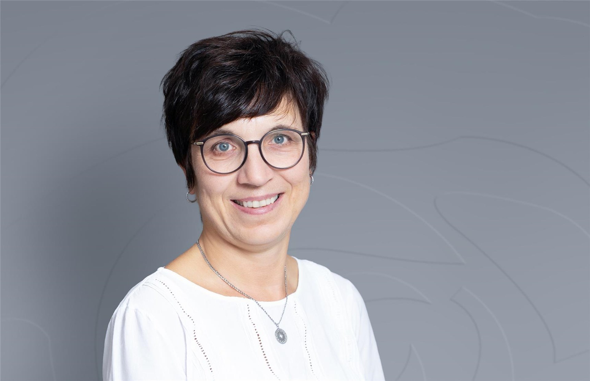 Frau mittleren Alters mit kurzen dunklen Haaren und einer Brille lächelt in die Kamera
